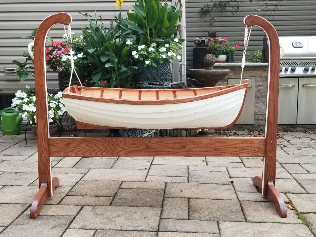 Cradle in the style of a rowboat made by Paul Musso. The cradle has a white outer hull and is hung from a frame by carefully tied ropes. The inside shows the careful craftsmanship by Paul.